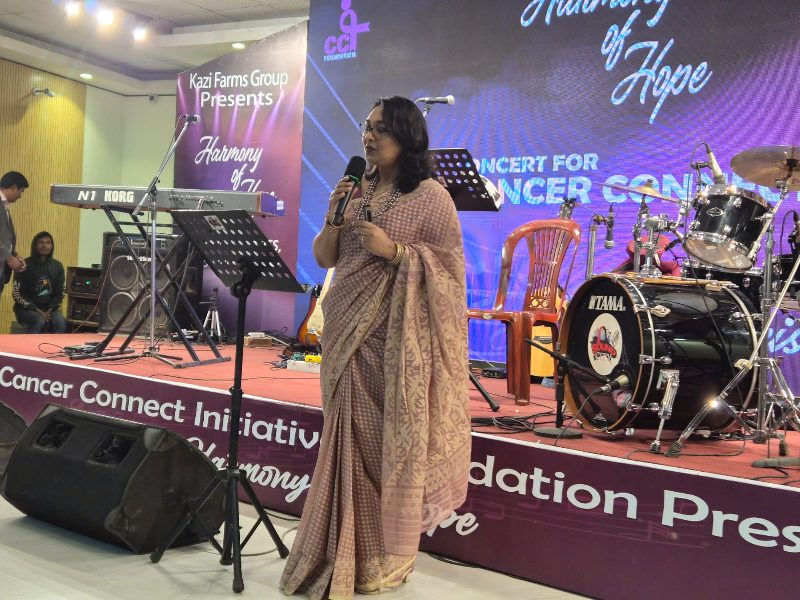 A speaker addressing the audience on stage at the Harmony of Hope concert for Cancer Connect
